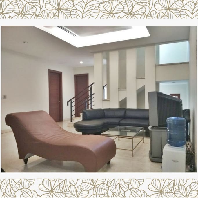 tampak ruang keluarga, ada sofa hitam & kursi santai warna cokelat. lengkap dengan TV