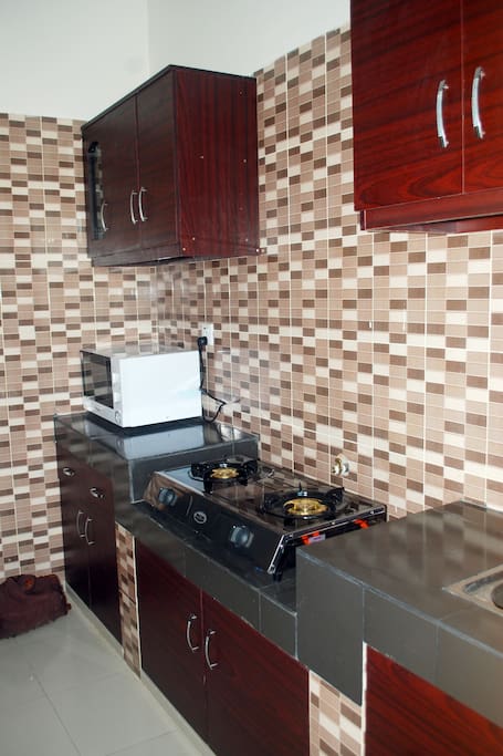 Kitchen with gas cooker, microwave, fridge, sink, store room, and cutlery.
