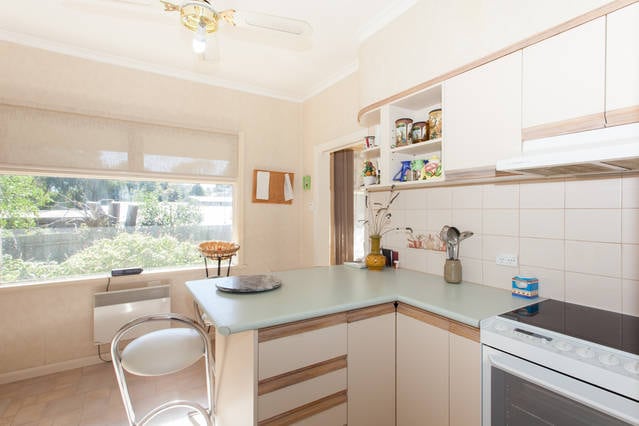 The kitchen features a modern design with light-colored cabinetry and a spacious countertop. A bar stool is positioned at the counter, while a window allows natural light to illuminate the room. Various kitchen items are neatly arranged on shelves, enhancing functionality.