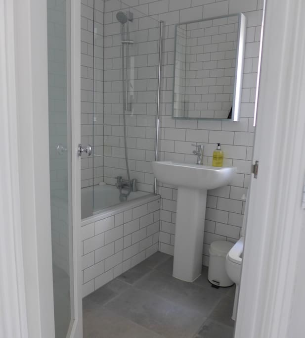 Fully tiled, new bathroom with shower and cabinet over sink which includes its own surround lighting for brightly lit shaving / make-up application!
