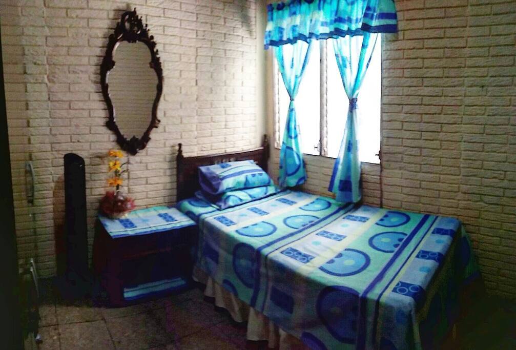 En esta foto pueden observar como luce la habitación, cuenta con su espejo, ventilador, mesa de noche, ventana, guardaropas y también encontraran una mesa donde podrán utilizar su computadora. Here you can see how our room looks like, it has a mirror, the bed, a fan, a night table, the window and you will also find a table to put your laptop in case you need it.