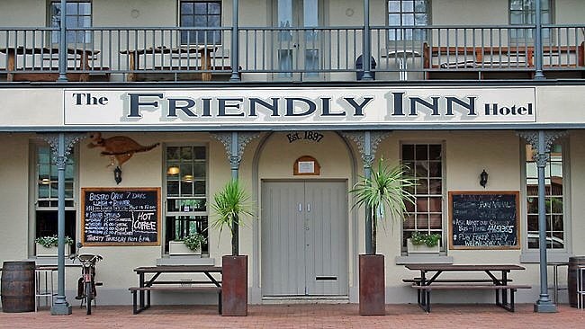 The Friendly Inn Hotel features a welcoming façade adorned with the establishment's name and establishment year. Potted plants flank the entrance, while wooden tables and benches provide outdoor seating options. Chalkboards display the menu and promotions, reinforcing a casual dining atmosphere.