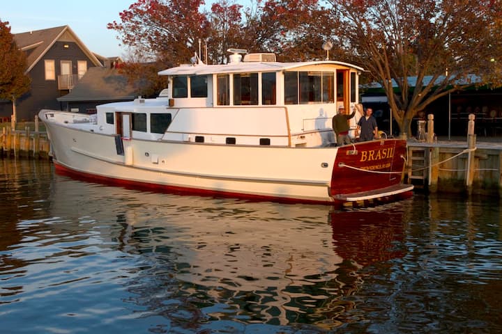 A yacht vacation rental in Rhode Island floats on the water with autumn foliage behind it