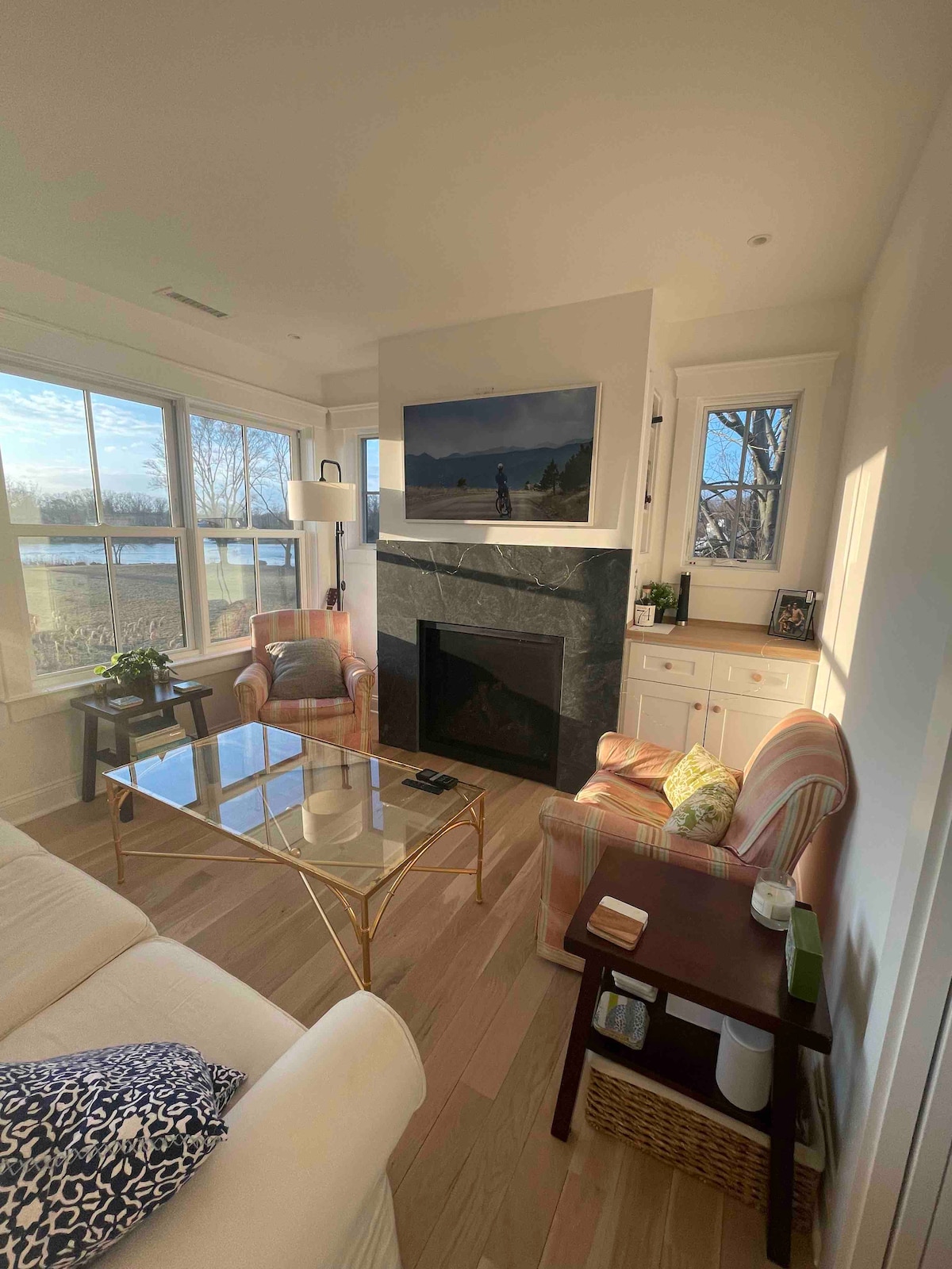 A cozy living area features large windows allowing natural light to fill the space. A modern fireplace is situated between the windows, complemented by a tasteful mantle. Two comfortable armchairs and a glass coffee table create an inviting seating arrangement.