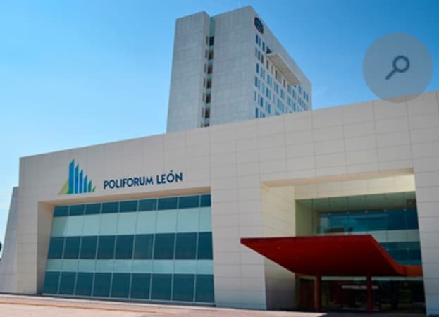 The image features a modern building showcasing the Poliforum León logo prominently on a white facade. The entrance is marked by a striking red canopy, contrasting with the glass windows that reflect the clear blue sky.