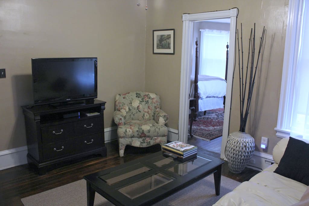 Bright living room offers oversized windows with shades, leather couch, 37" flat screen tv, comfortable chair.