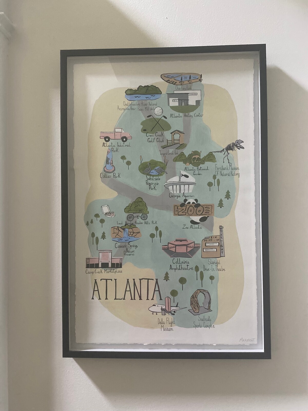 A framed illustration of Atlanta featuring whimsical landmarks and attractions. The design uses soft colors with detailed drawings, including notable buildings and natural features, arranged geographically. The title 'ATLANTA' is prominently displayed at the bottom in bold lettering.