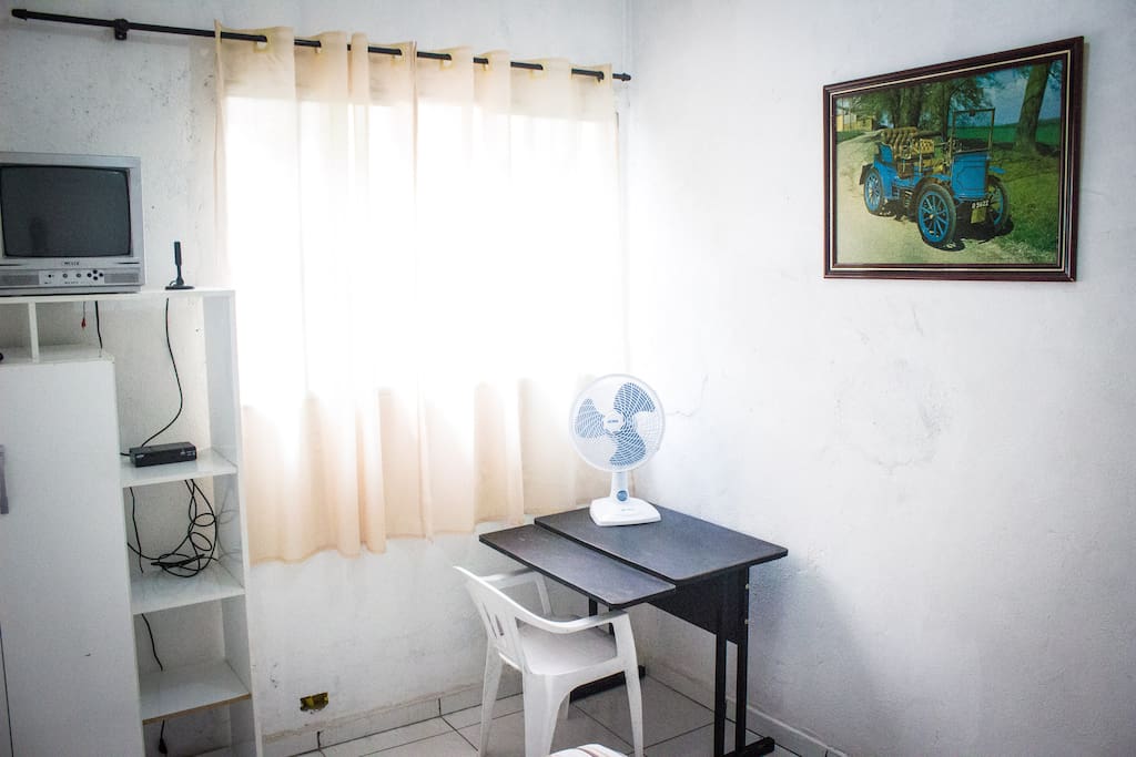 Imagem complementar do quarto com vista para TV, ventilador e escrivaninha