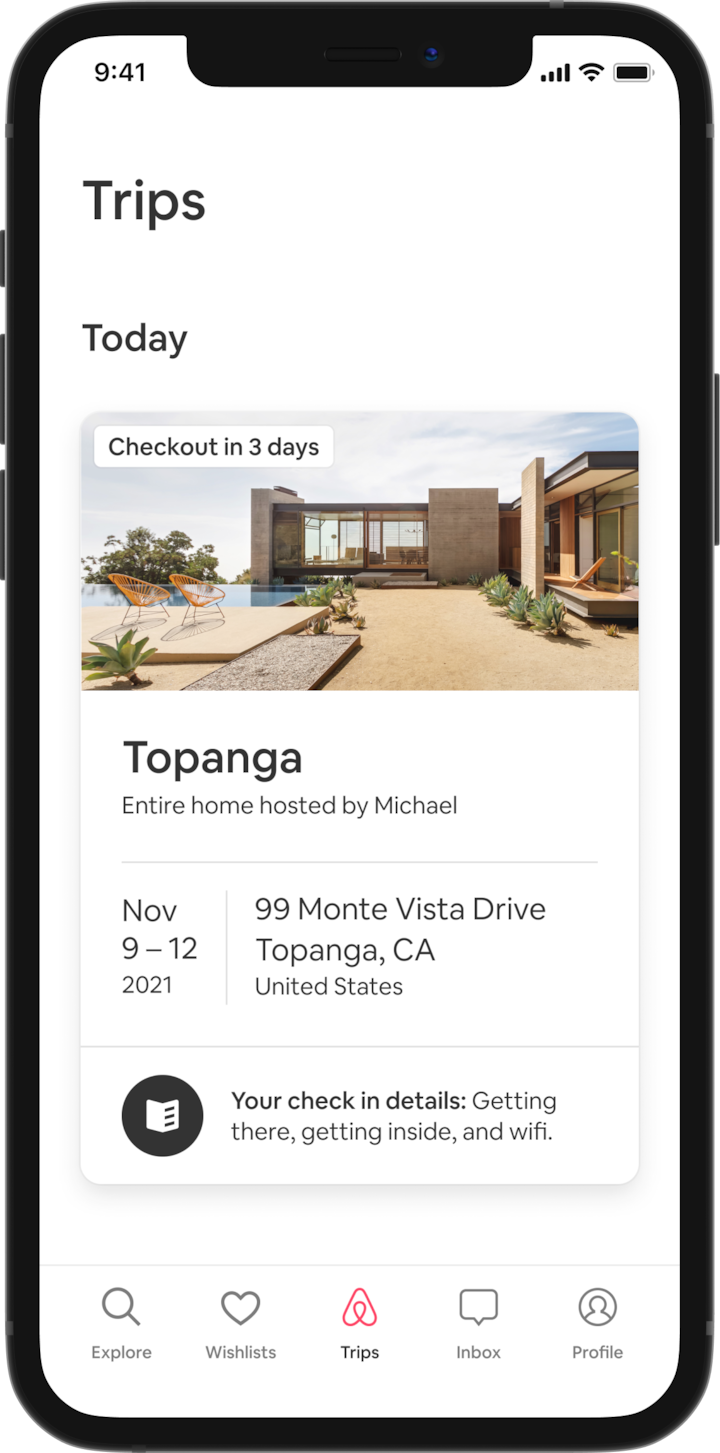 A cell phone displays a guest’s Trip tab which shows an upcoming trip. Under a heading that reads ‘Today’ there is an image of an A-frame house, and under this, there are details about the guest’s booking—the listing name, the name of the Host, the address, and the dates for the trip. At the bottom of the screen there is a button that reads: “Your check-in details. Getting there, getting inside, and wifi.”