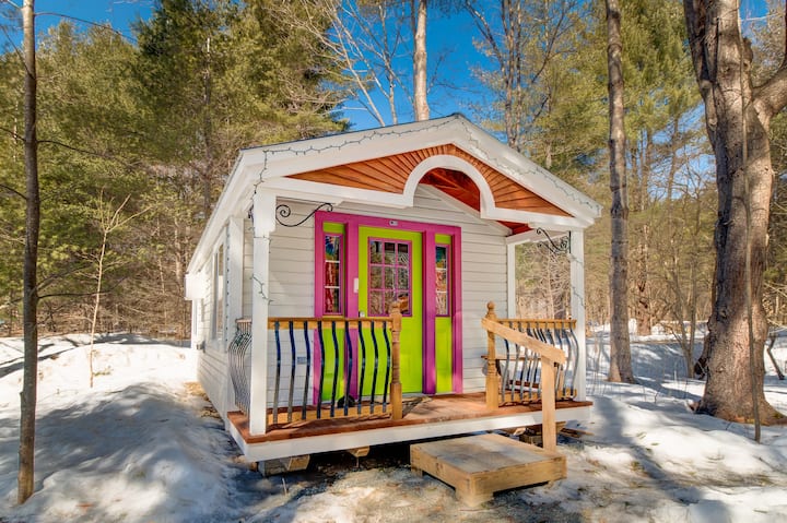 A pink and green accented tiny house Airbnb in Vermont sits on a small snowy hill