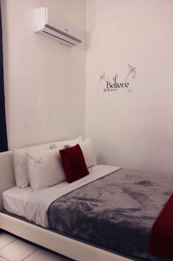 Vista al área de habitación la cual cuenta con una cama Queen size, mesita de noche, y todas sus almohadas y sabanas.