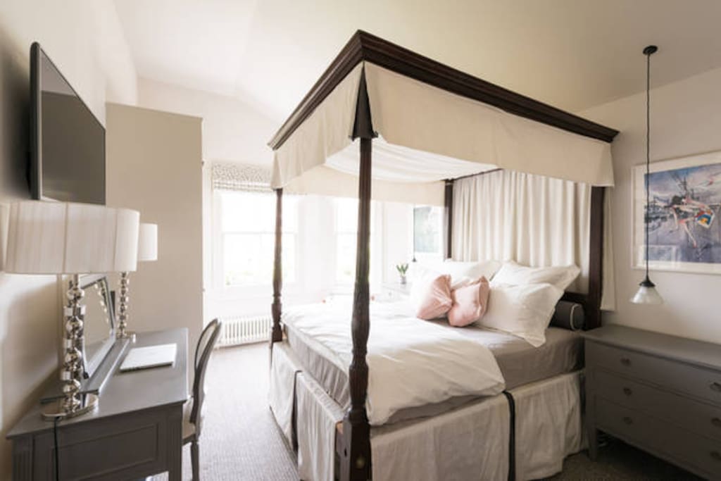Guest Bedroom with antique four poster bed, dressing table, wall mounted flatscreen smart TV with cable.