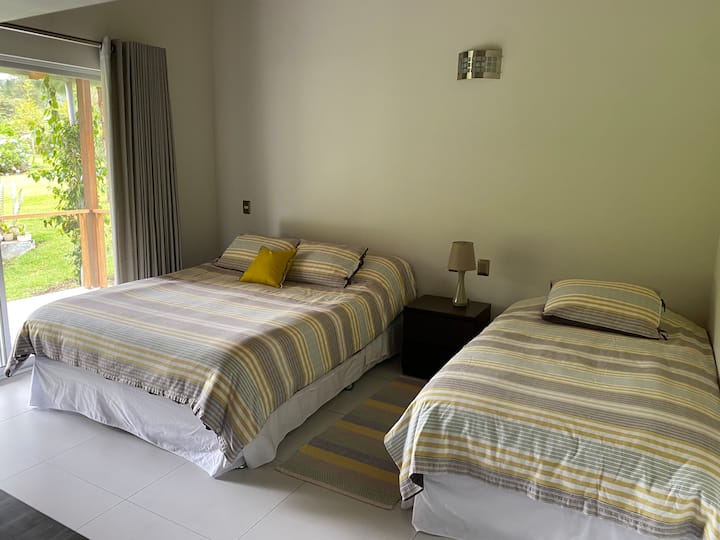 Dormitorio con cama queen y cama de plaza y media, baño incorporado. 