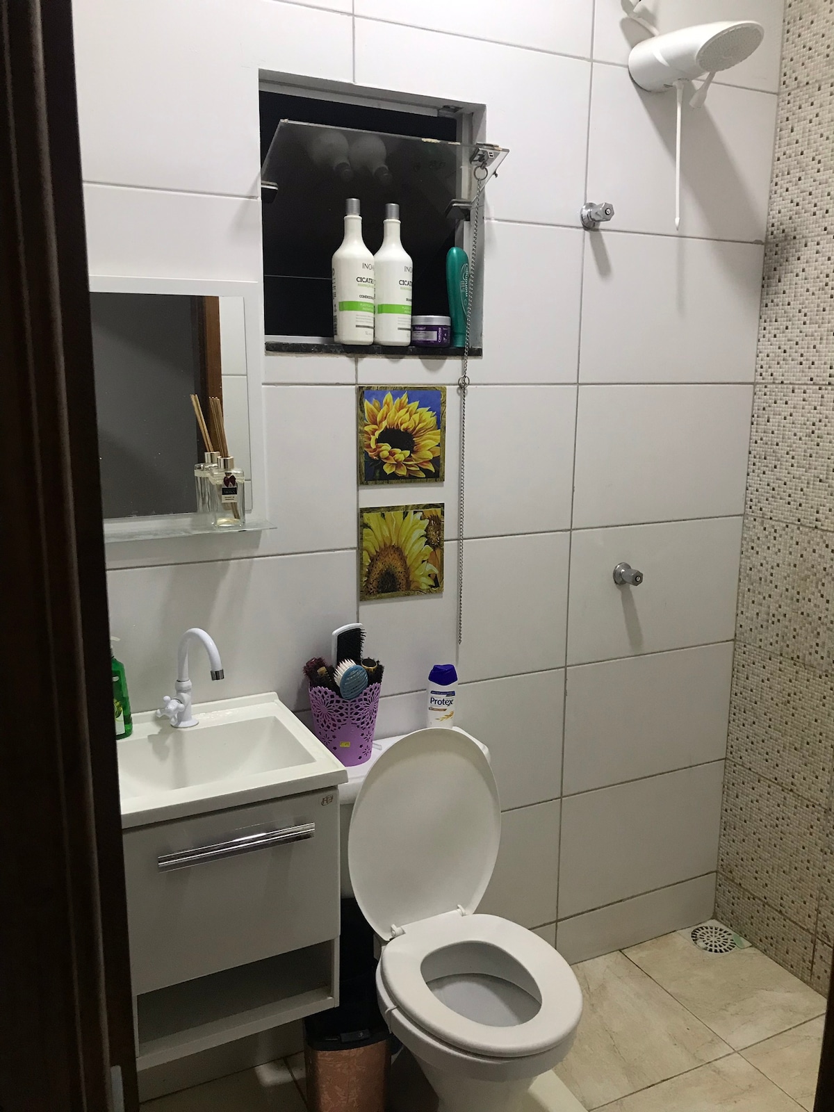 A compact bathroom is equipped with essential fixtures, including a toilet and a sink adorned with complementary toiletries. A small mirror is mounted above the sink, and a decorative arrangement of products is displayed on a shelf. Natural light filters in through a window.