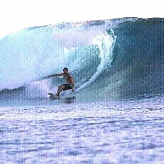 A surfer is captured riding a large wave, with water cascading around him. The ocean reflects shades of blue, enhancing the dynamic movement of the wave. The surfer appears focused as he navigates the powerful swell, creating a sense of adventure and excitement.