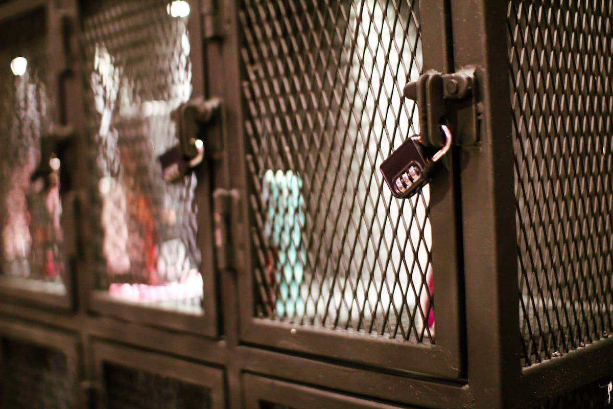 A series of metal storage cabinets are visible, featuring mesh wire fronts secured with combination locks. The cabinets are placed against a blurred background, suggesting a functional and secure area for personal items.