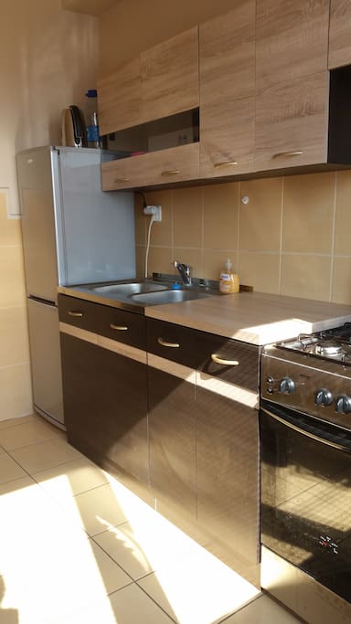 Spacious kitchen with fridge, stove, kettle, pots and pants and a sitting area.