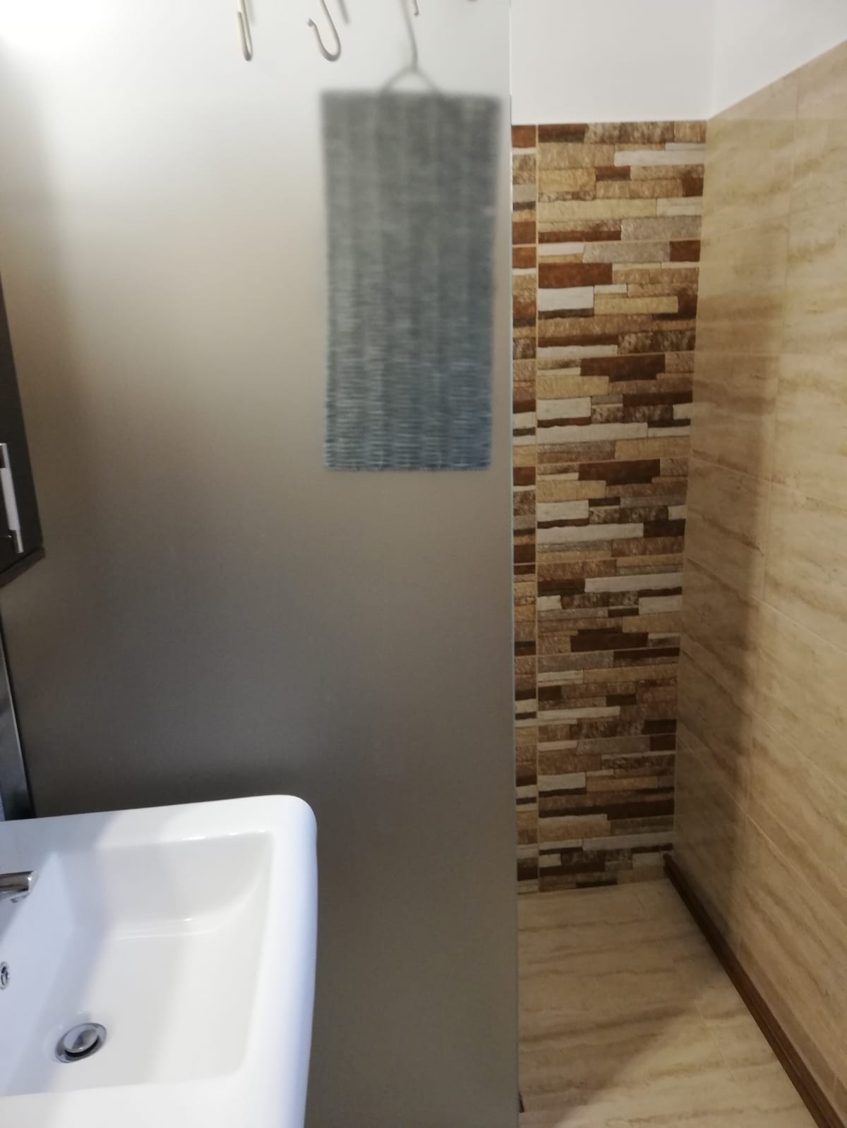 A modern bathroom is featured with a sink and a patterned tile wall. The textured wall behind is composed of varying shades of brown and beige tiles, while a smooth, neutral-toned wall creates a serene atmosphere.