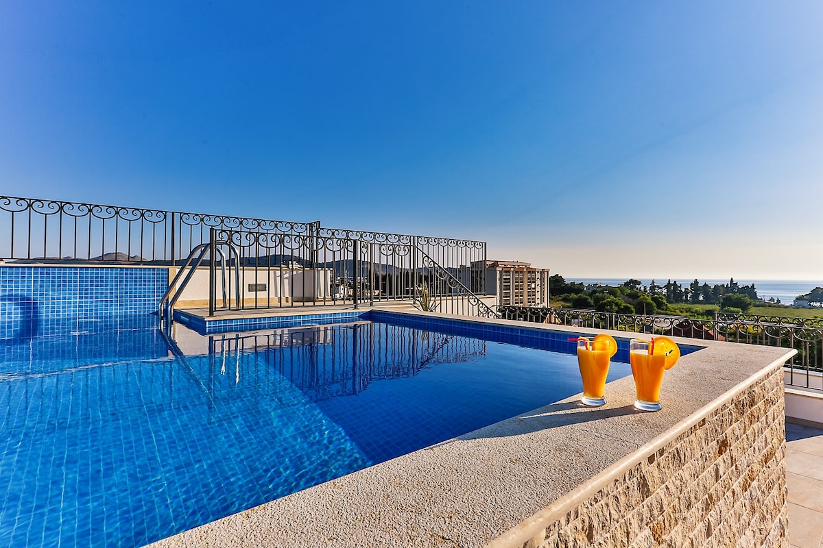A rooftop pool offers a serene escape with clear blue water and a scenic view of the surrounding landscape. Two glasses are placed on the ledge, inviting relaxation and enjoyment of the outdoor setting.