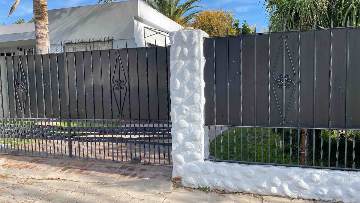A gated entrance features a combination of smooth white stone and dark metalwork. The clean lines of the gate provide a sense of structure, surrounded by lush greenery and palm trees, enhancing the welcoming ambiance of the property.