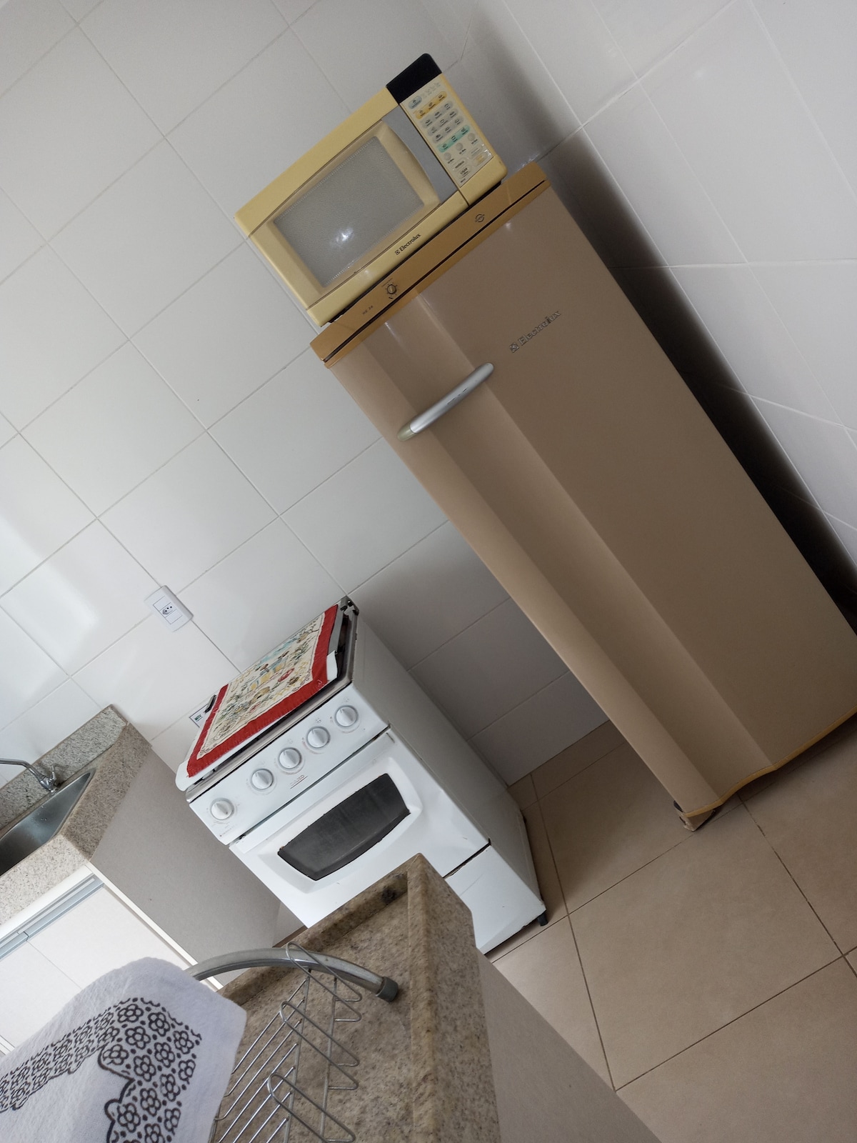 The kitchen features a compact stove and an oven, alongside a beige refrigerator. A microwave is placed on top of the refrigerator, contributing to the space's functional design. The countertops are constructed from a light-colored stone, enhancing the kitchen's modern appearance.
