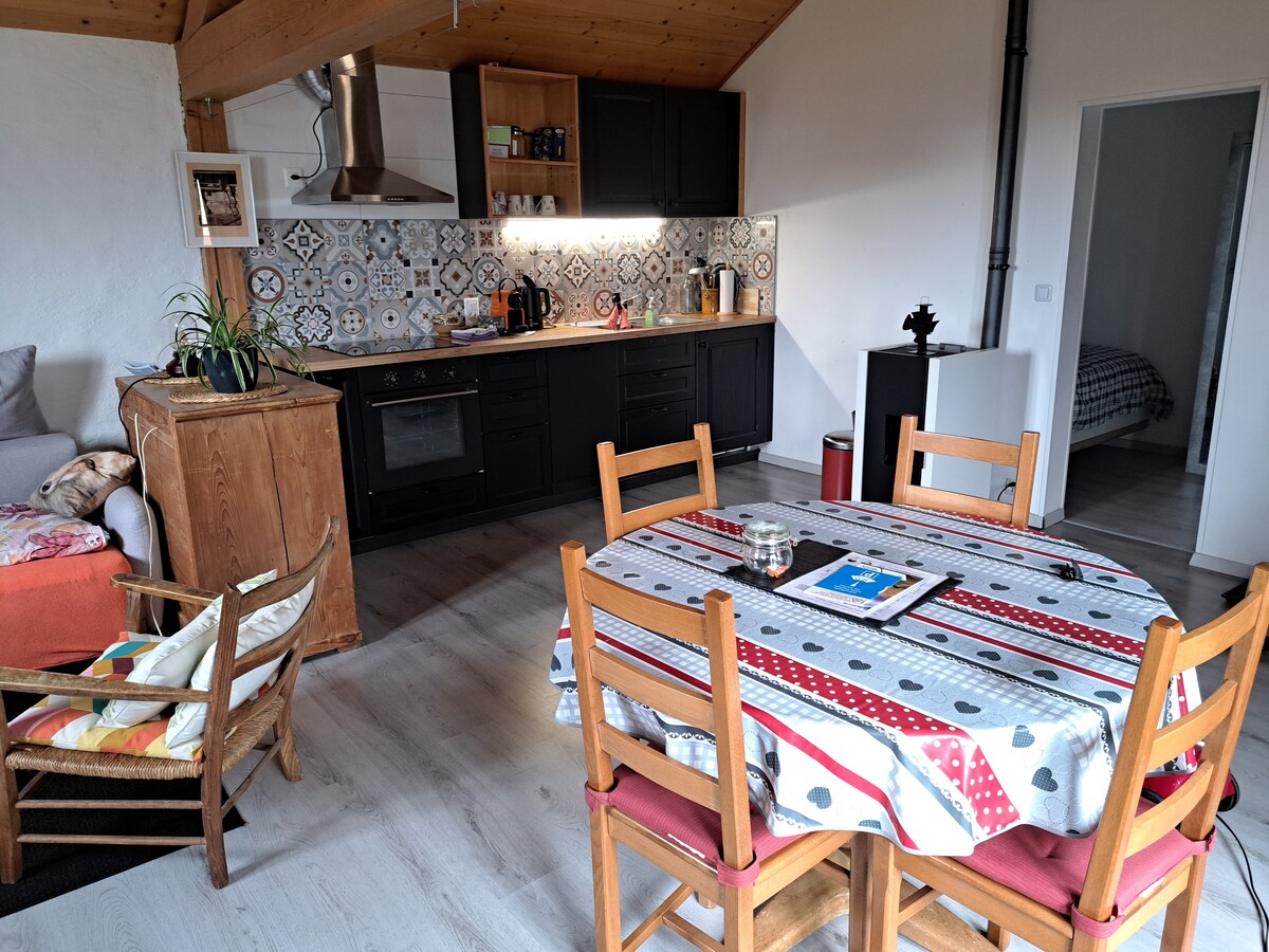A modern kitchen features black cabinetry and decorative backsplash tiles, with essential appliances including an oven and coffee machine. A wooden dining table is surrounded by six chairs, while a cozy seating area includes a sofa and a wooden storage unit.