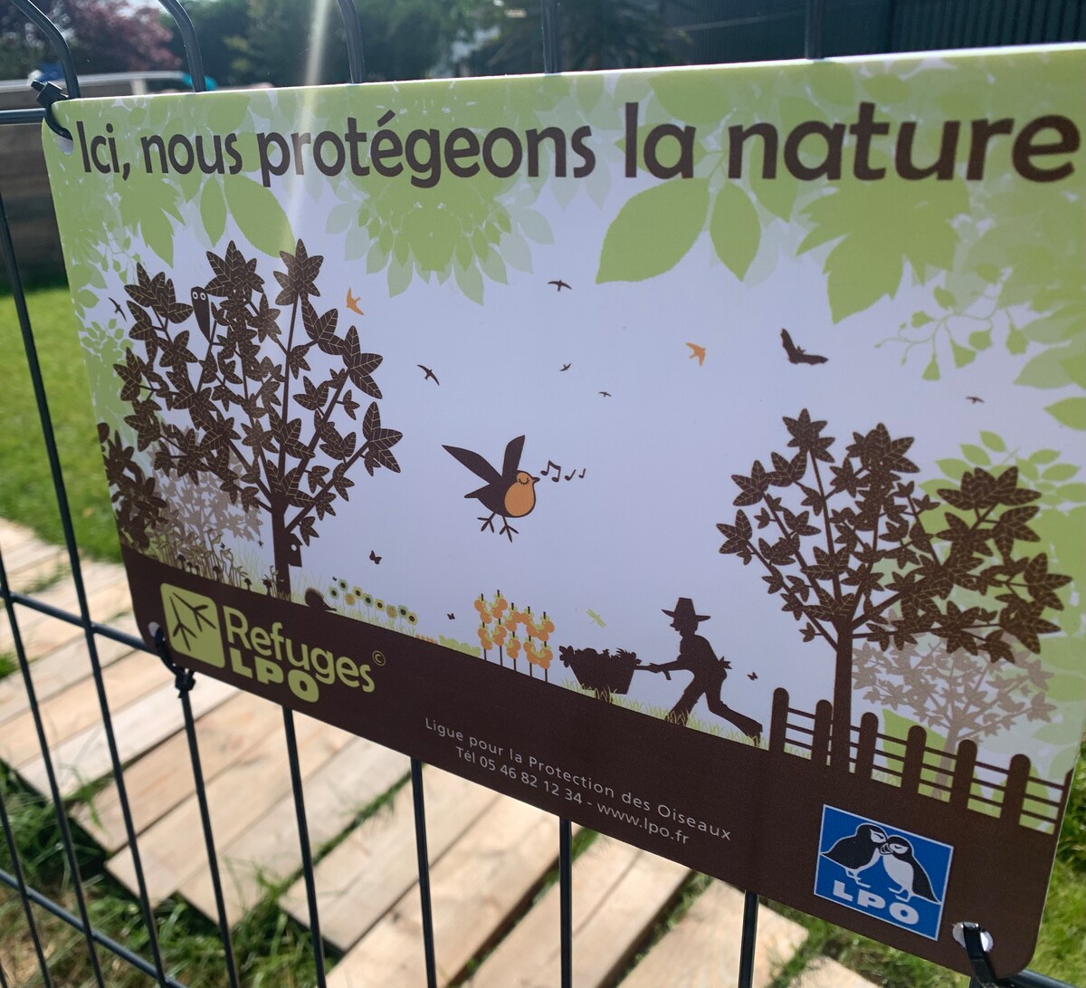 A vibrant sign is displayed within the garden, promoting nature conservation. The illustration features a bird perched among stylized trees, with a person tending to plants. Subtle greens and browns create a harmonious blend, emphasizing the commitment to protecting the environment.