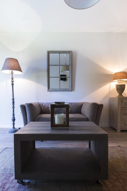 The living area features a comfortable gray couch positioned across from a wooden coffee table. A candle is placed on the table, surrounded by a decorative lantern. Two lamps provide soft lighting, enhancing the warm ambiance.