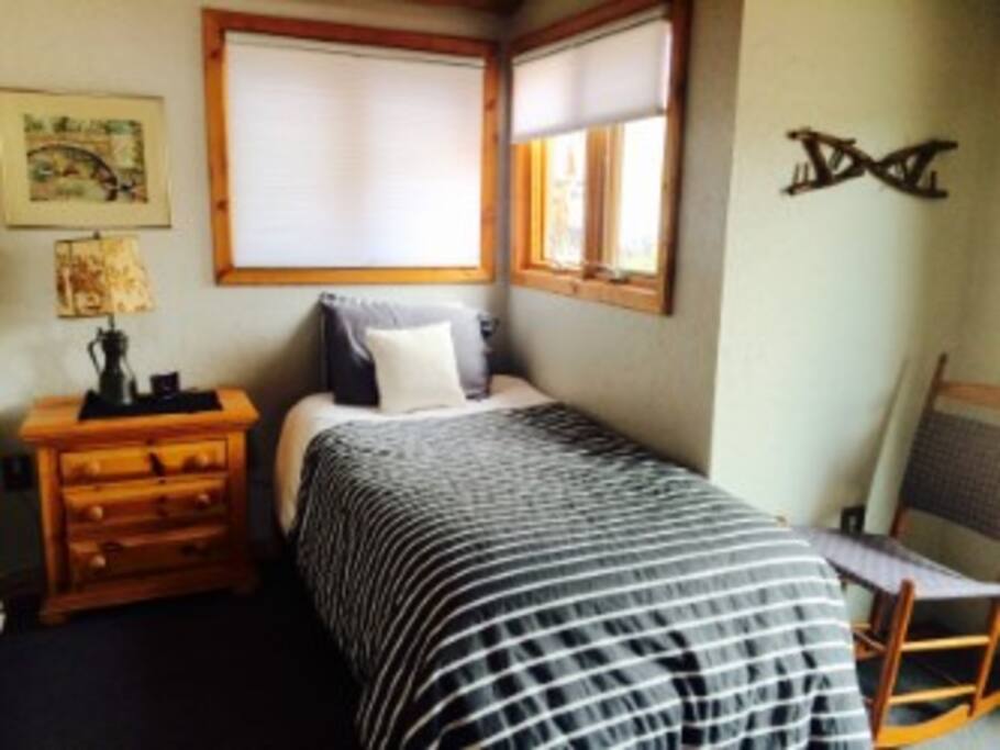 West twin bed with luxury linens, night stand and windows fog cross ventilation and plenty of light. There is a ceiling fan.