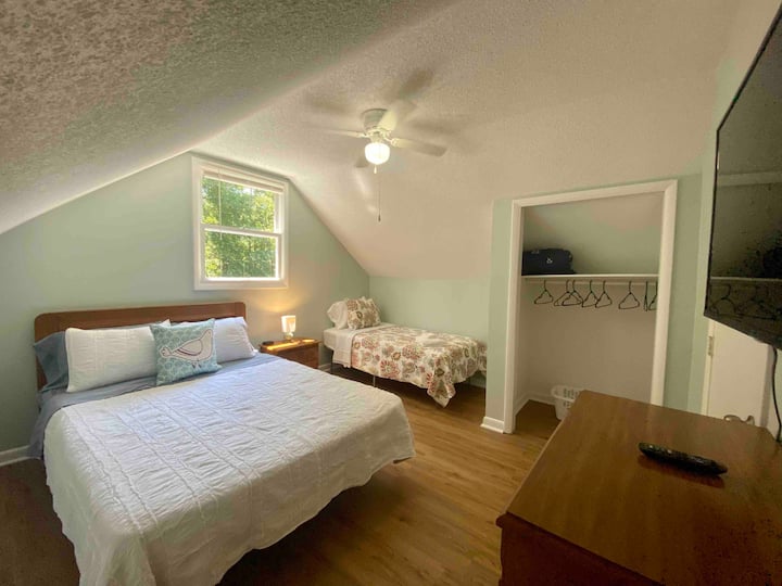 Lado izquierdo del dormitorio de arriba, cama tamaño queen y cama individual, televisión y armario. Estación de carga de teléfono USB en la mesita de noche.