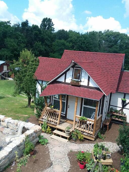 An aerial view of the Storybook Cottage--- above the porch, a gnome sits in his rocking chair by candlelight watching over the cottage garden.