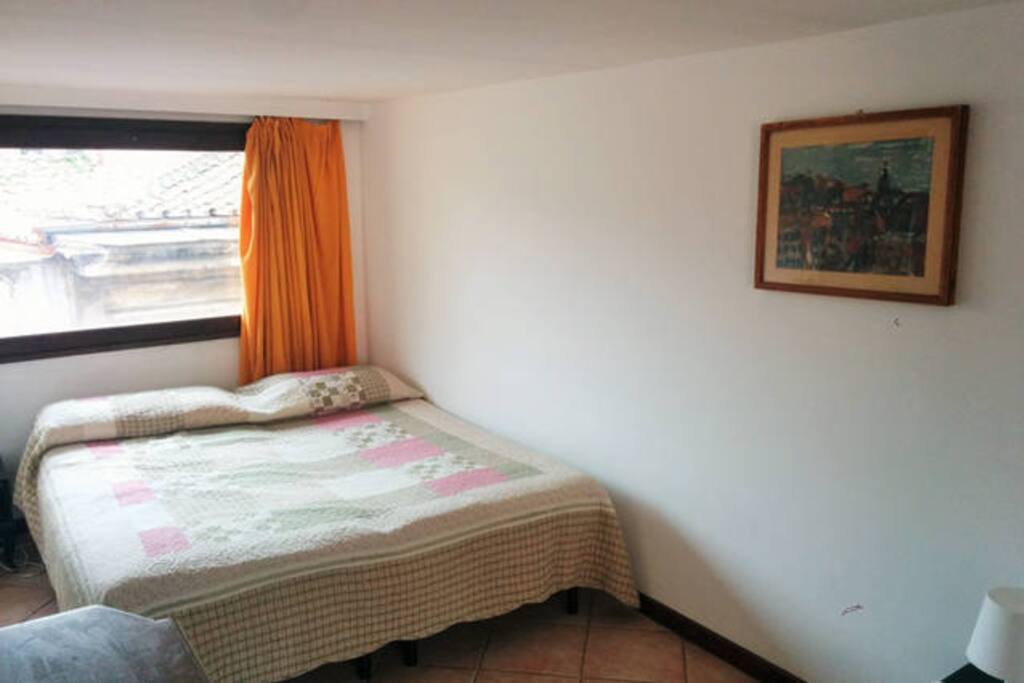 The bedroom is flooded with sun and light through the large window looking over the roofs of trastevere