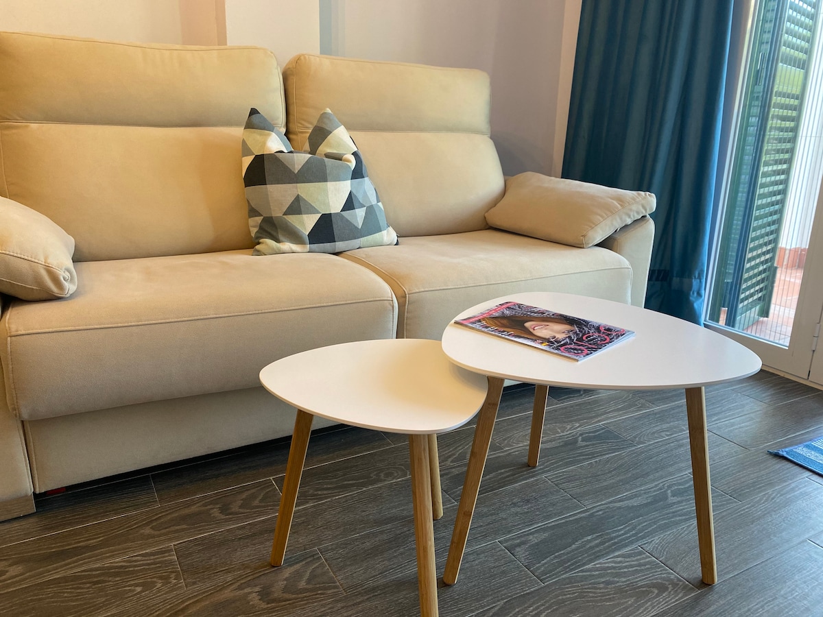 A comfortable seating area is featured, showcasing a light-colored sofa paired with a patterned cushion. Two modern side tables, one larger and one smaller, are positioned in front of the sofa. A magazine rests on the surface of the larger table, complementing the space.