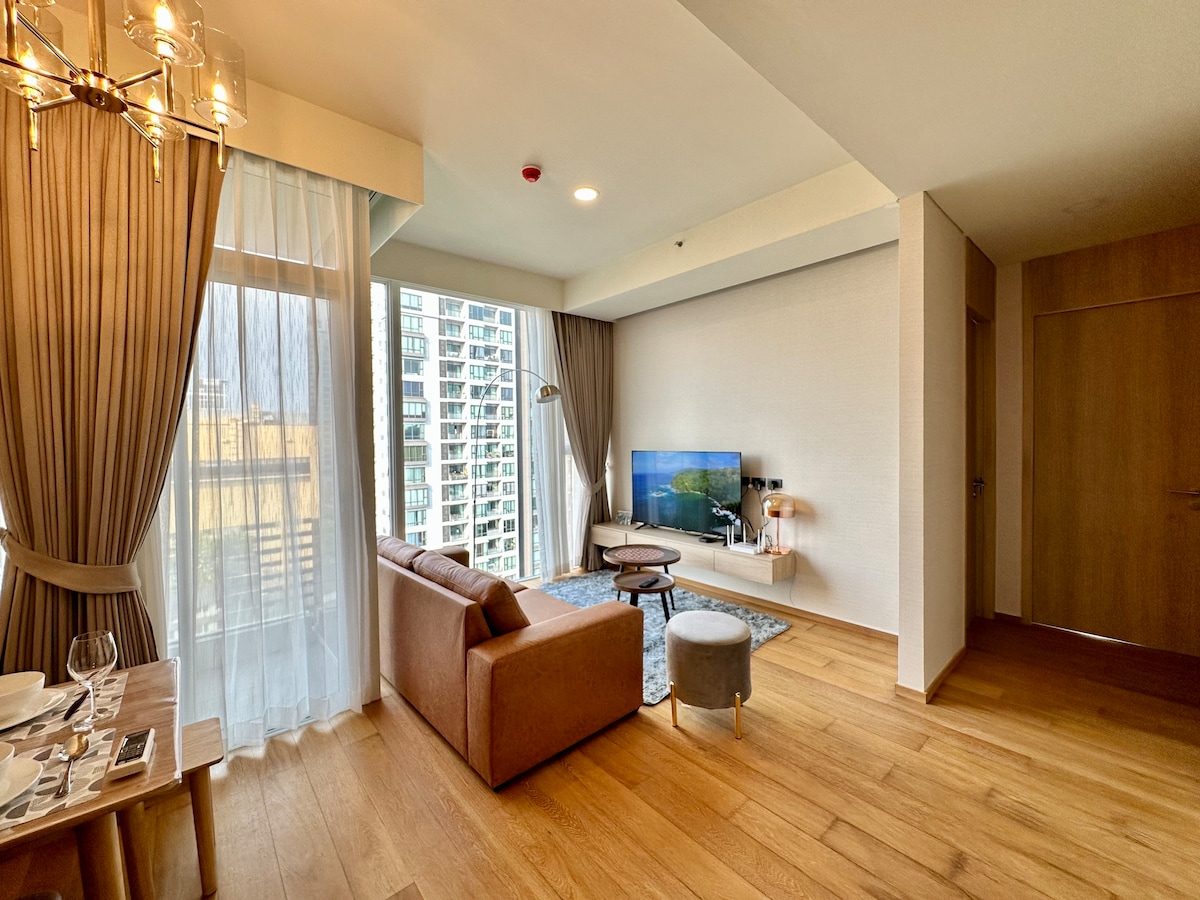 A modern living area is featured with warm wooden flooring and large windows that allow natural light to fill the space. A comfortable sofa is positioned near a stylish entertainment unit, while a dining table set for four enhances the inviting atmosphere.