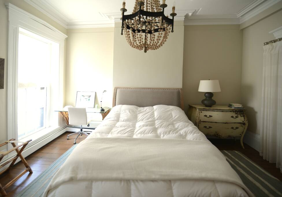 wide-angle view of bedroom, w/chandelier, writing desk we/view of public garden, stand for suitcase, wood floors, and carpeting