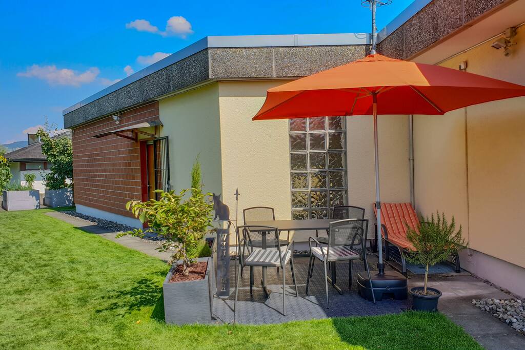 Eigener Gartensitzplatz mit Sonnenschirm und Grill. Sowohl für die Stühle wie auch den Liegestuhl stehen bequeme Kissen zur Verfügung. Im Hintergrund ist unser Quittenbaum zu sehen. Ebenso haben wir im Garten 2 Apfel- und einen Birnbaum.