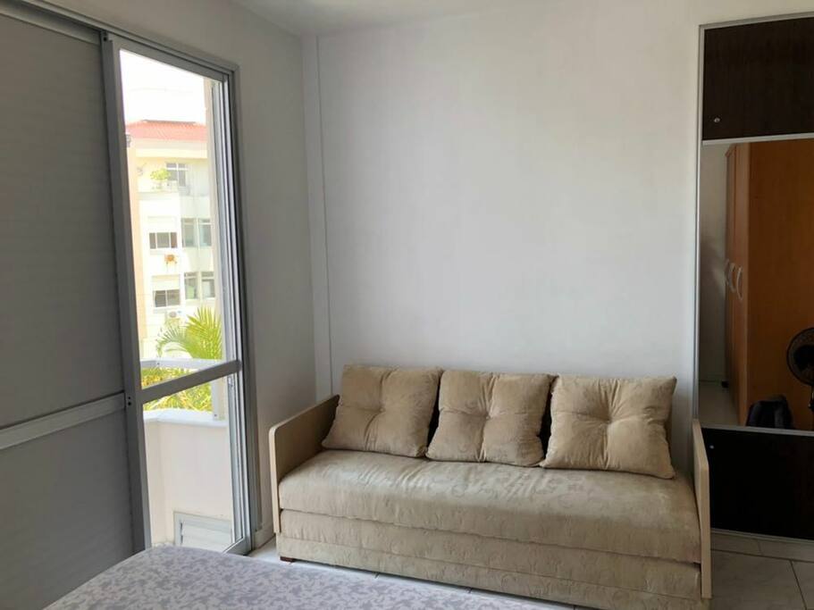 Suíte com sacada, ar condicionado, ventilador, cama de casal e sofá cama