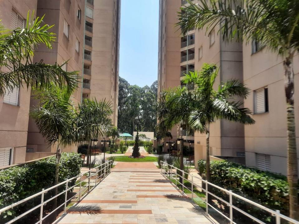 A landscaped pathway is flanked by palm trees, leading towards a central green area with outdoor seating. The surroundings include two residential buildings, creating a peaceful atmosphere. An inviting lawn area is visible in the background, providing a spacious outdoor setting.