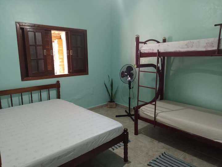 Spálňa (2) s manželskou posteľou, poschodovou posteľou, ventilátorom, zásuvkou so štyrmi zásuvkami a oknom s výhľadom na predný dvor domu.