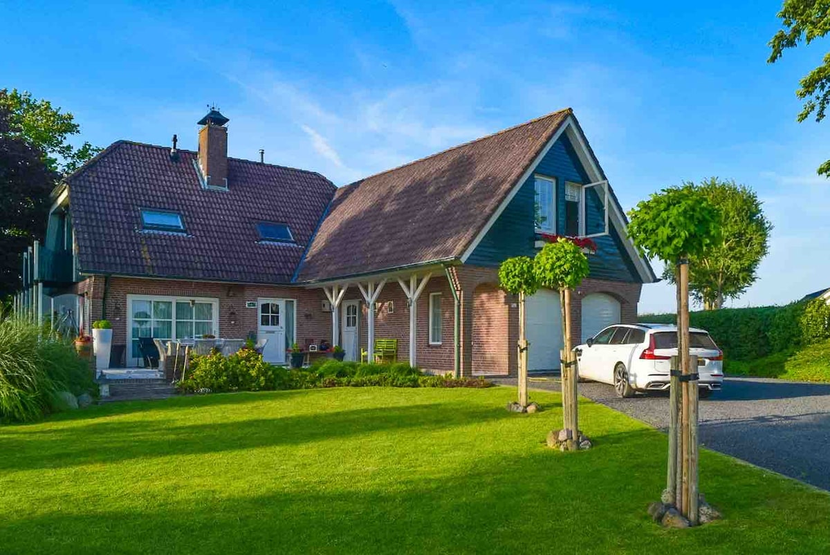 The exterior of the property showcases a well-maintained garden with manicured grass and decorative trees. A brick and wood house features a distinct sloped roof, multiple windows, and a garage. A parked car is visible on the driveway, inviting a sense of home.