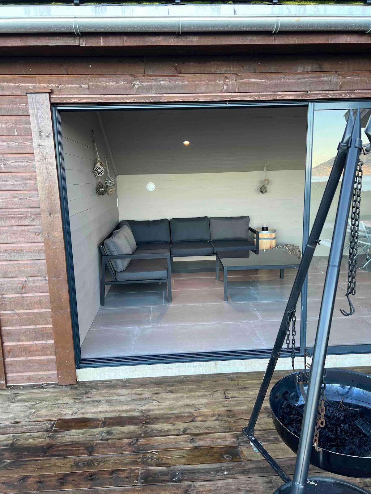 An outdoor seating area is visible through large glass doors, featuring a dark sectional couch and a matching coffee table. The surrounding wood deck enhances the relaxed setting, while a hanging swing adds a cozy touch to the space.