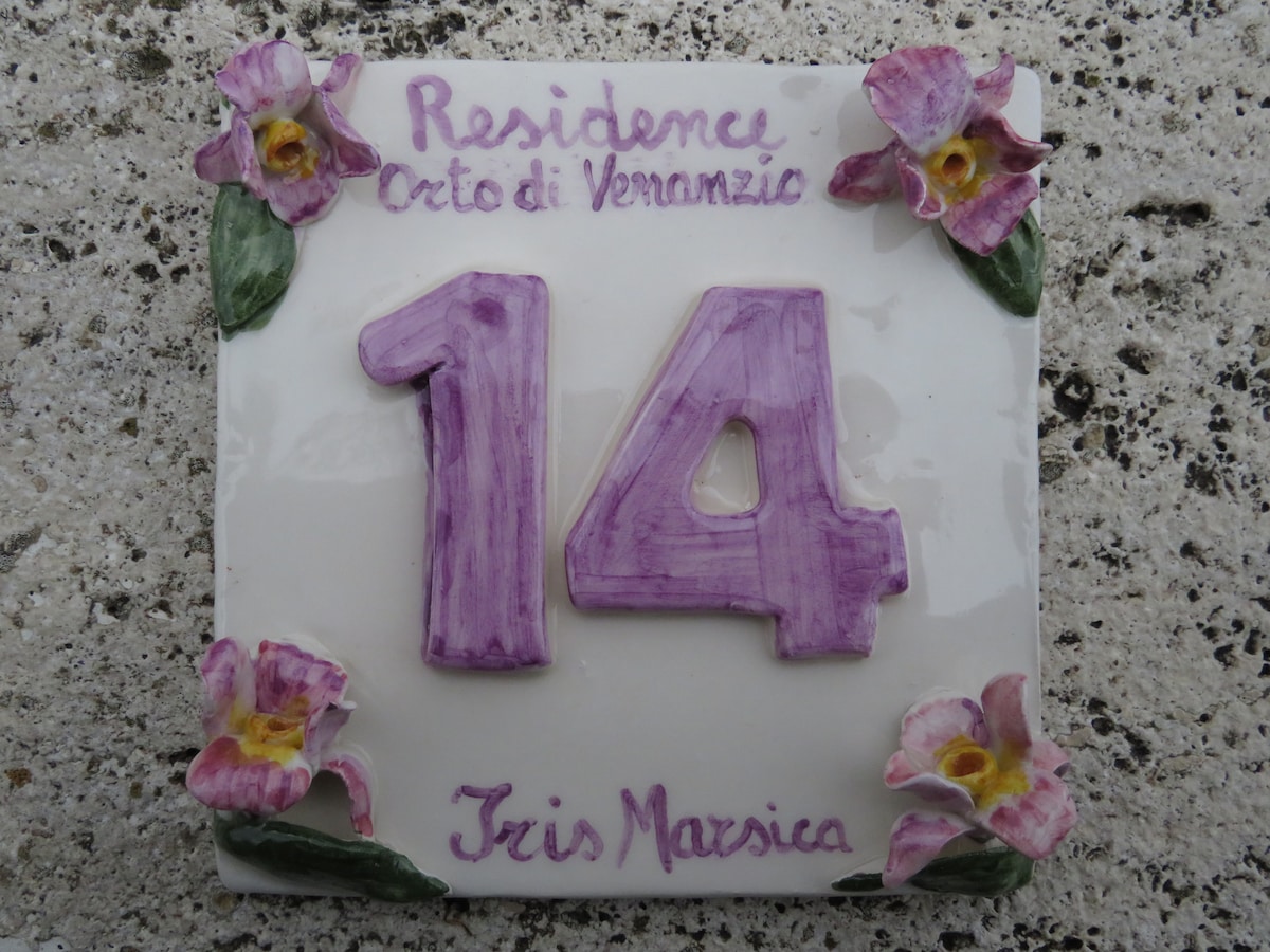 A decorative ceramic plaque displays the number 14, framed by floral designs in shades of purple. The inscription reads 'Residence Orto di Venanzio' along with the name 'Iris Marzica,' providing a welcoming touch to the property's entry.