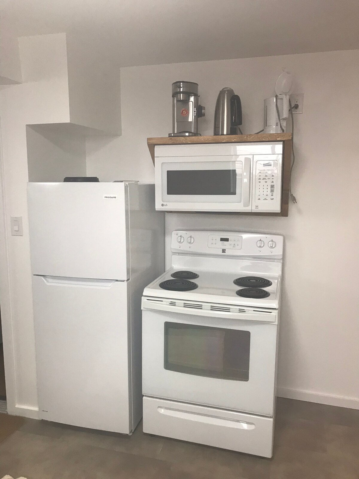 A neat kitchen area is presented, featuring a white refrigerator, an electric stove, and a microwave mounted above. A countertop holds a coffee maker and a kettle, providing essential appliances for meal preparation and enjoyment.
