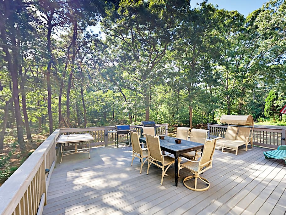 The spacious deck includes ample lounge seating, al fresco dining, and forested surroundings.