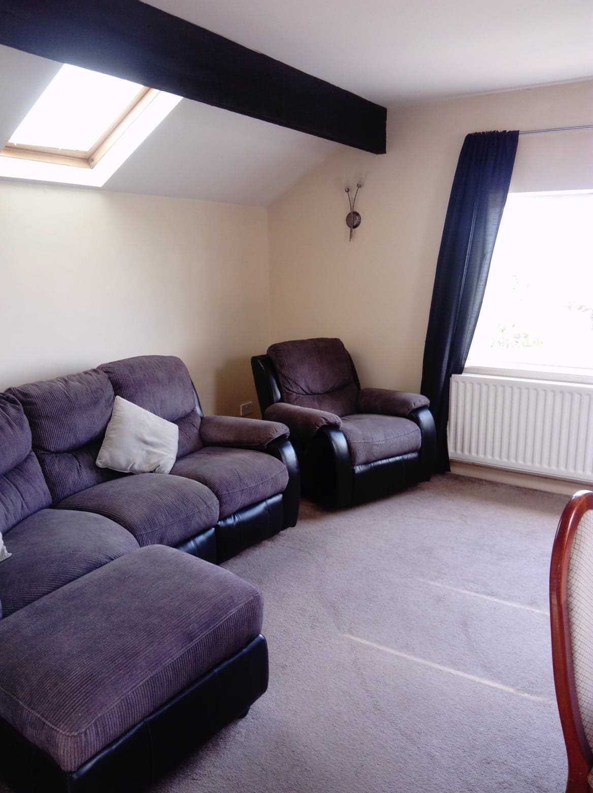 A comfortable seating area presents two dark leather recliners and a plush sofa, inviting relaxation. Natural light enters through the skylight and window, while soft, neutral tones create a calm atmosphere. A radiator is positioned beneath the window, contributing to the cozy feel.