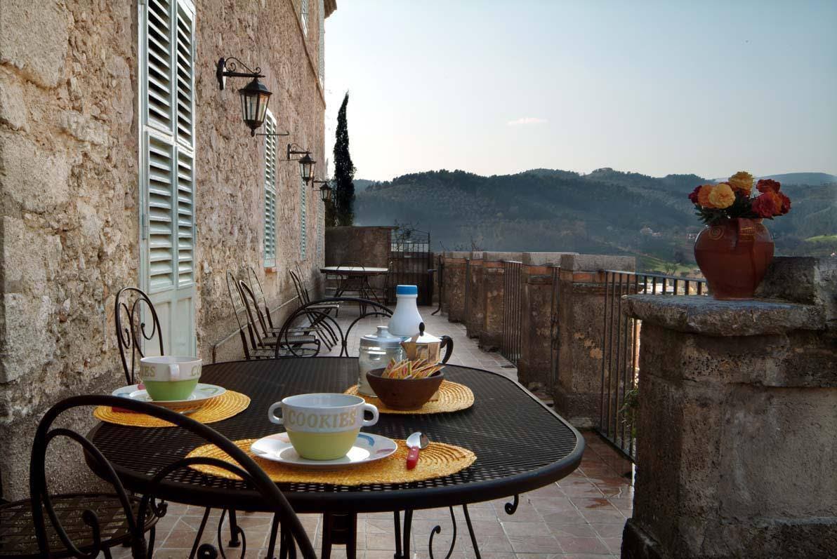 An outdoor terrace is presented, featuring a round table set for breakfast. Two bowls are placed next to a container of cookies and a bottle of milk. Scenic views of rolling hills and distant mountains are visible in the background, adding to the tranquil setting.
