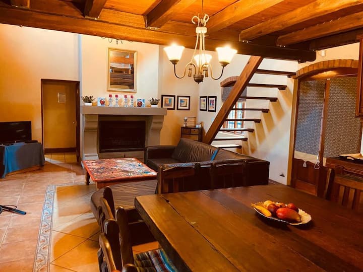 Salón y comedor de planta abierta con chimenea. Escaleras que suben a la zona del loft.