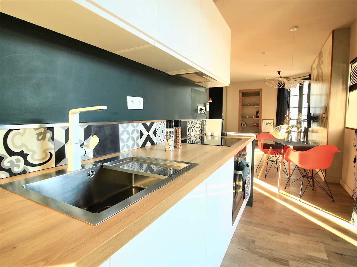 The kitchen features a modern design, highlighted by a spacious wooden countertop and a stainless steel sink. Colorful tiles adorn the backsplash, complementing the cabinetry. An inviting dining area is visible, showcasing decorative chairs and a light fixture that adds to the contemporary style.