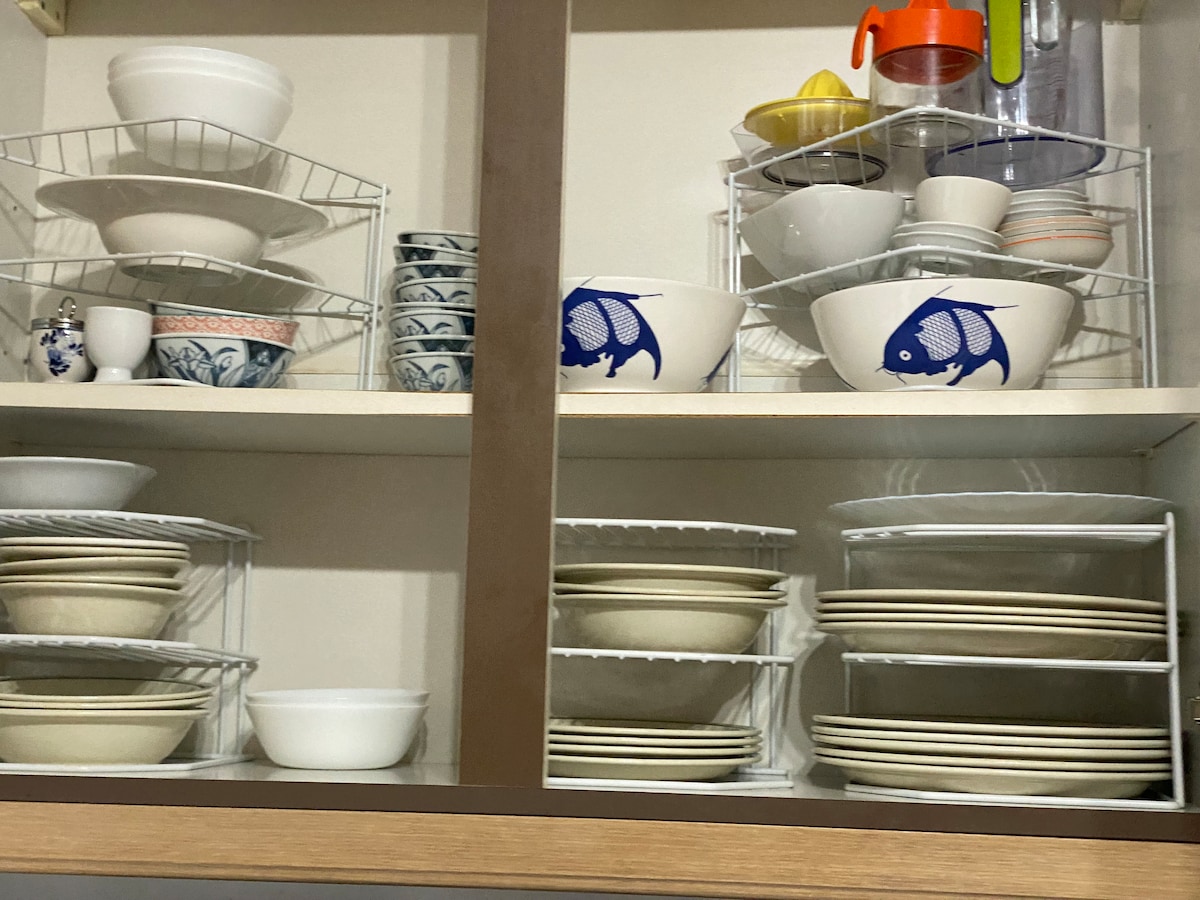 The image displays a neatly organized kitchen cabinet featuring various dishware. Multiple shelves hold ceramic bowls, plates, and cups, with distinctive blue fish designs on select pieces. An assortment of styles and sizes provides suitable options for dining needs.