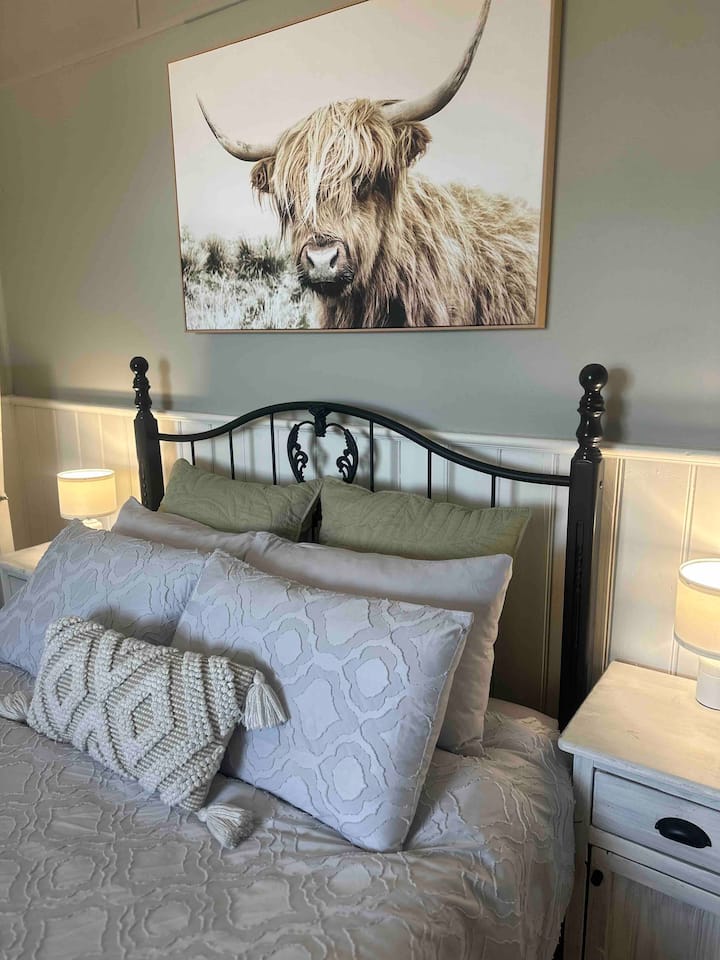 The first queen bedroom is a cozy haven featuring an antique style bed, memory foam topped mattress and soft linens. The rustic decor creates a private space to unwind in comfort. The room features a desk, monitor, full-length mirror and wardrobe.